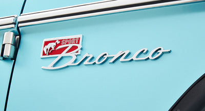 Raised chrome and red 'Sport Bronco' emblem on light blue classic Ford Bronco door panel
