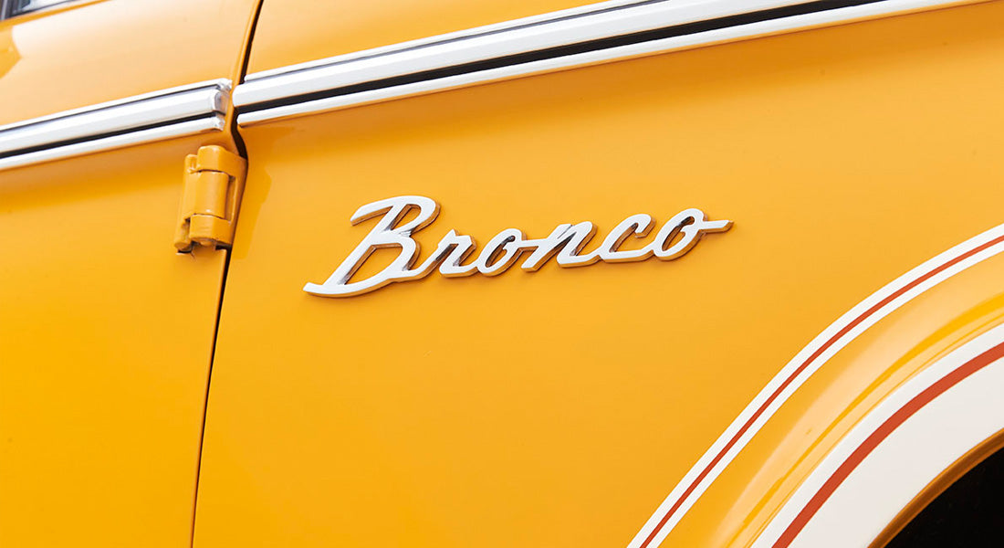 Classic Ford Bronco emblem on yellow vehicle with white and orange striping