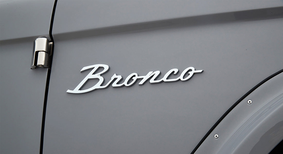 Classic Ford Bronco emblem mounted on smooth light gray body panel near door hinge