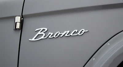 Classic Ford Bronco emblem mounted on smooth light gray body panel near door hinge