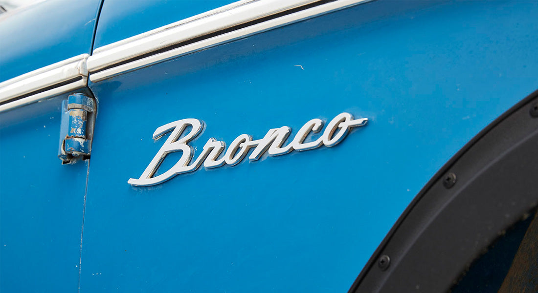 Close-up of Classic Ford Bronco silver emblem on blue vehicle body panel