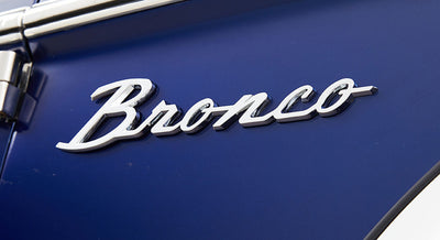 Chrome 'Bronco' emblem on blue vehicle surface near a door hinge