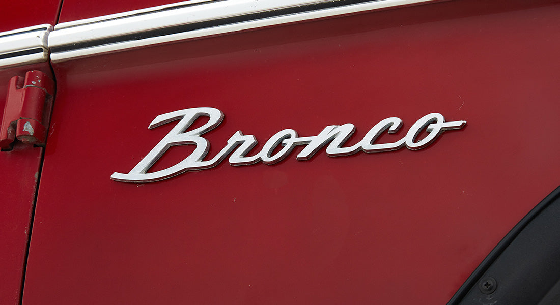 Silver Bronco emblem mounted on the red exterior of a Classic Ford Bronco door panel