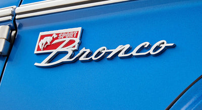 Classic Ford Bronco chrome emblem on blue painted vehicle body with 'Sport' label and running horse.