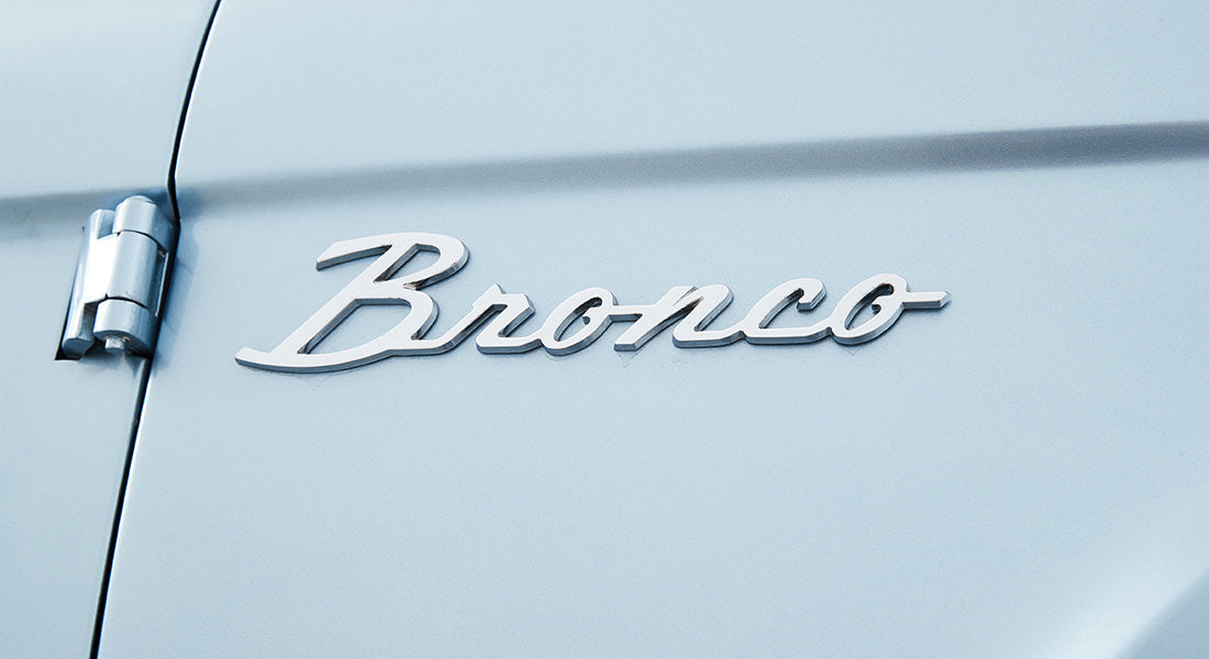 Chrome script emblem reading 'Bronco' on light blue Classic Ford Bronco exterior