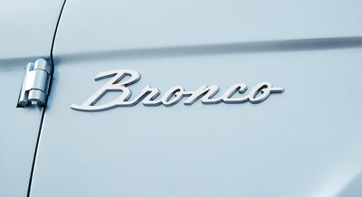 Chrome script emblem reading 'Bronco' on light blue Classic Ford Bronco exterior