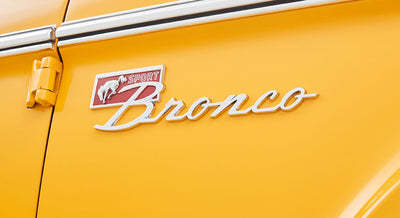 Close-up of Classic Ford Bronco in yellow-orange with chrome 'Sport Bronco' emblem on door