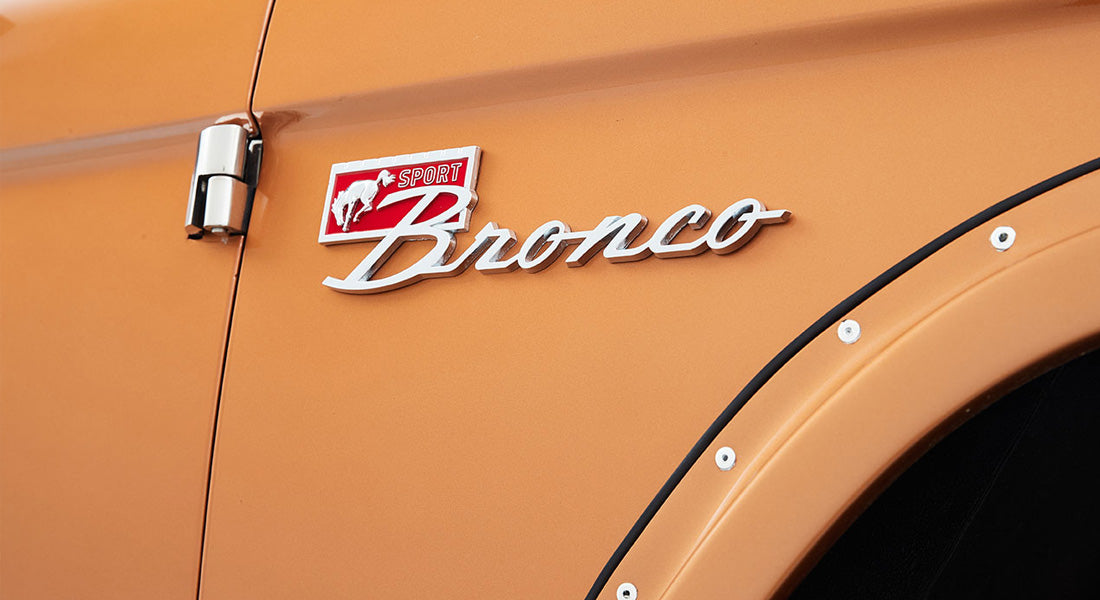 Close-up of Classic Ford Bronco in orange with chrome 'Sport Bronco' emblem and riveted fender flare