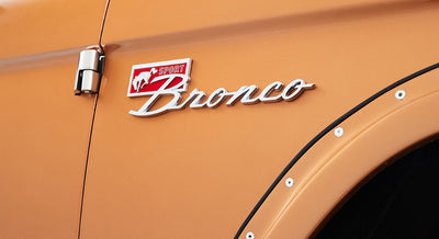 Close-up of Classic Ford Bronco in orange with chrome 'Sport Bronco' emblem and riveted fender flare