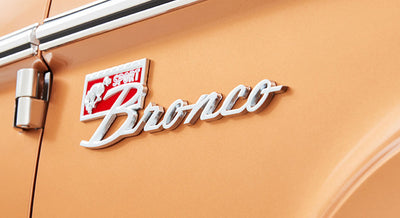 Classic Ford Bronco Sport emblem on orange vehicle exterior near door hinge