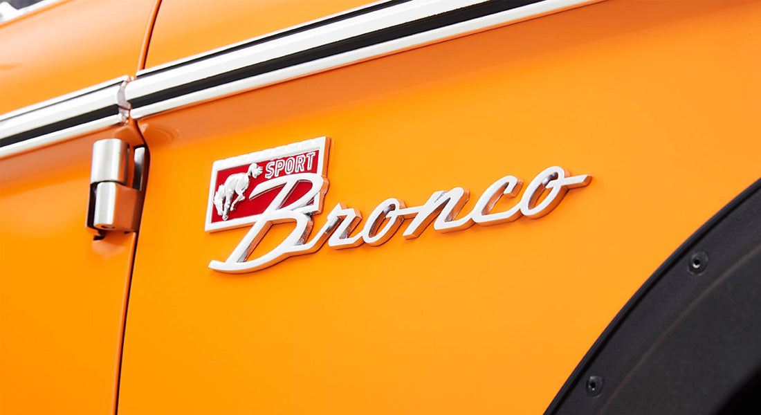 Chrome Sport Bronco emblem on orange vehicle exterior with door hinge visible