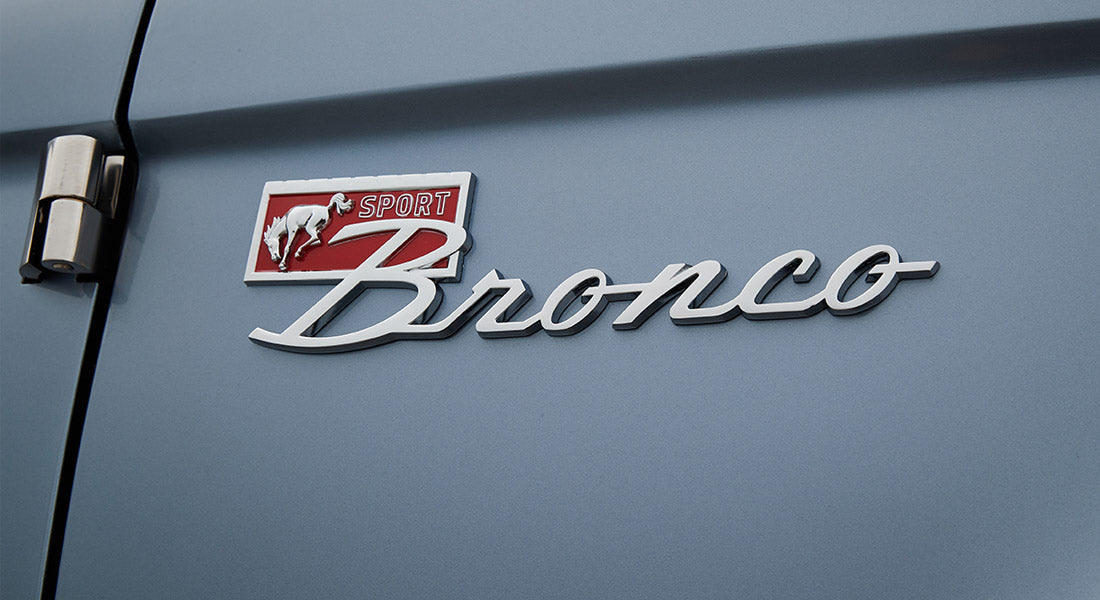 Silver and red Classic Ford Bronco emblem on a light blue painted exterior panel
