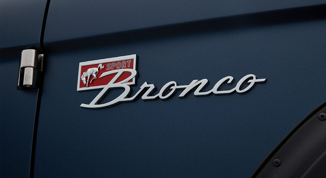 Metal bronco emblem with red 'Sport' badge on blue body panel of Classic Ford Bronco