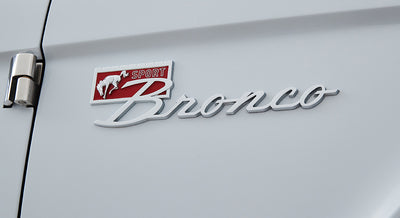 Chrome Classic Ford Bronco Sport emblem with red background on light gray vehicle body near door hinge