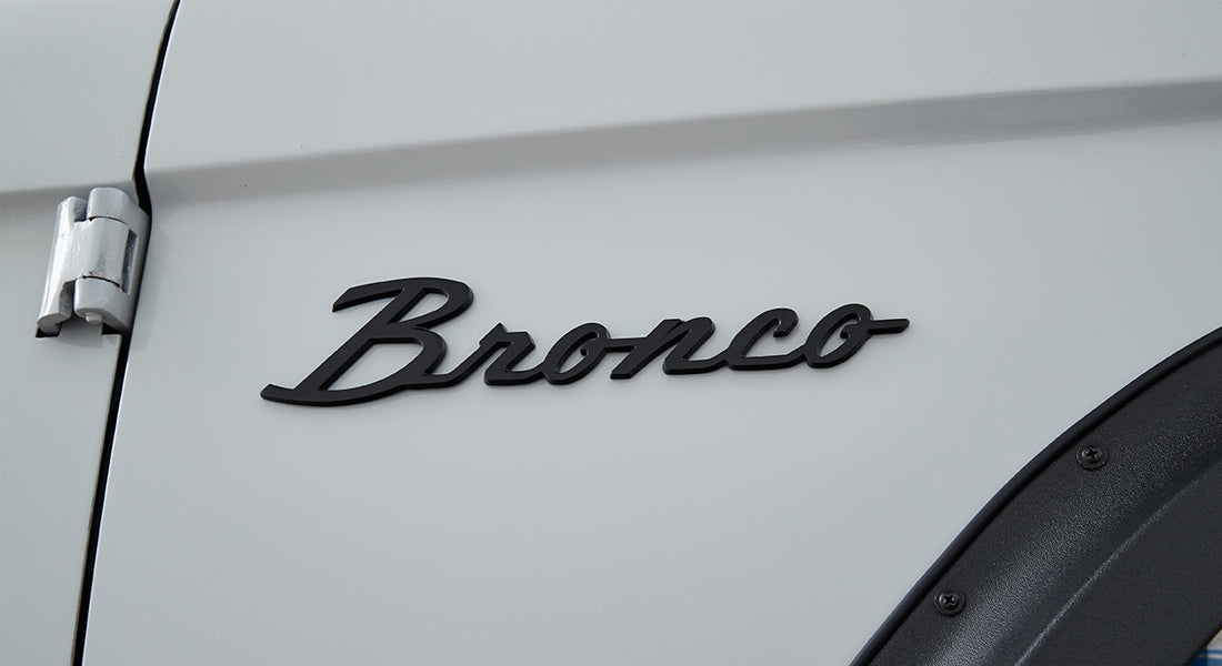 Matte black Classic Ford Bronco emblem on white vehicle door near hinge