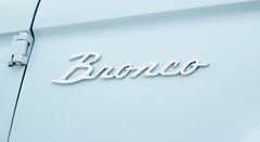 Chrome 'Bronco' emblem on the side door of a light blue Classic Ford Bronco