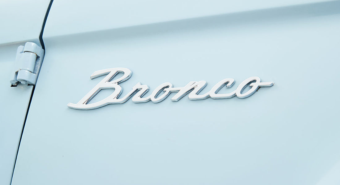 Chrome 'Bronco' emblem on the side door of a light blue Classic Ford Bronco