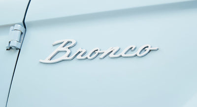 Chrome 'Bronco' emblem on the side door of a light blue Classic Ford Bronco