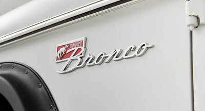 Classic Ford Bronco chrome emblem on white exterior near black fender flare