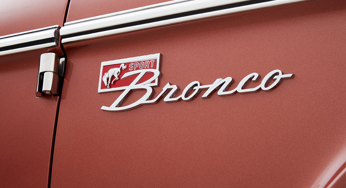 Classic Ford Bronco side emblem reading 'Sport Bronco' on metallic red door panel