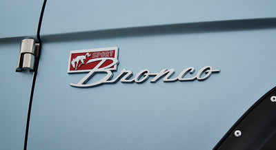 Chrome Classic Ford Bronco emblem with red and white sport badge on light blue vehicle body