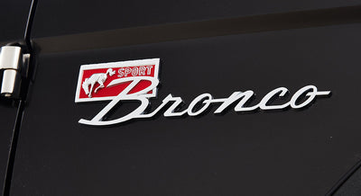Raised chrome and red 'Sport Bronco' emblem on black classic Ford Bronco door panel