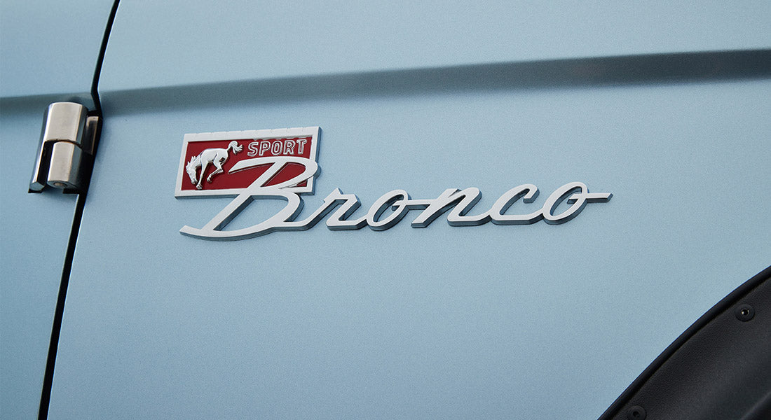 Silver Classic Ford Bronco emblem with a running horse and 'Sport' badge on a light blue vehicle panel