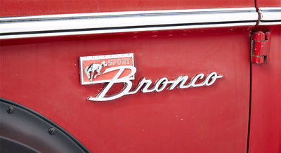 Close-up of red Classic Ford Bronco emblem with Mustang horse and script lettering on side panel.