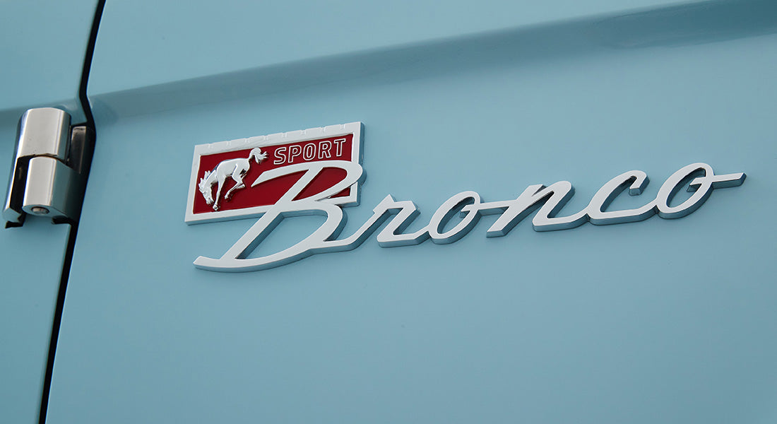 Classic Ford Bronco chrome emblem with red and white background on light blue vehicle body.