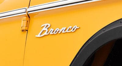 Close-up of chrome Bronco emblem on yellow Classic Ford Bronco vehicle body