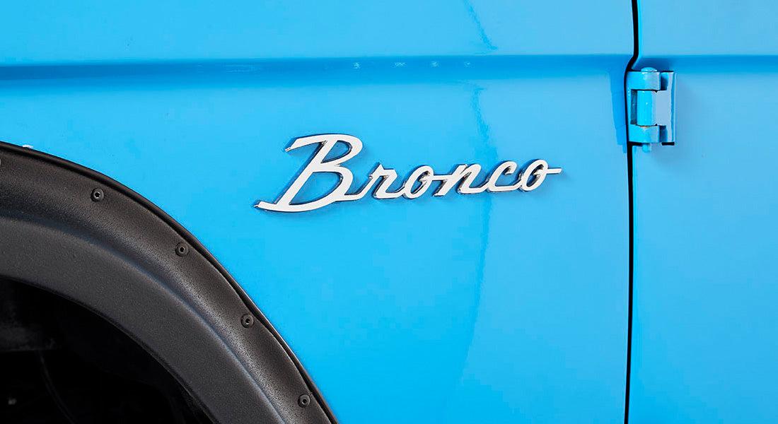 Close-up of Classic Ford Bronco emblem on blue side panel with part of the door hinge and fender flare