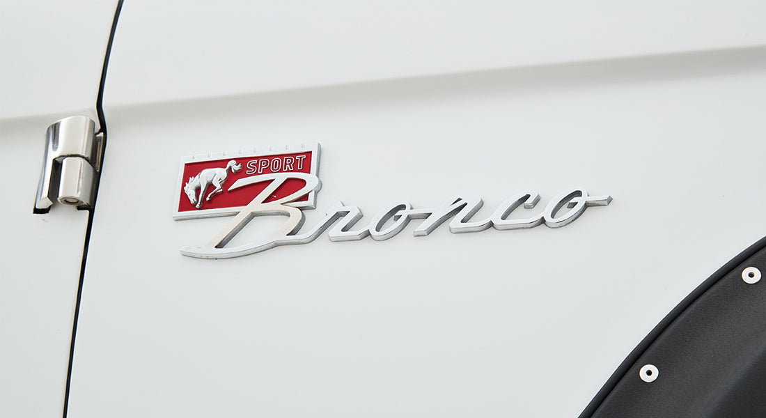Close-up of Classic Ford Bronco emblem on white vehicle body near door hinge