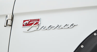 Close-up of Classic Ford Bronco emblem on white vehicle body near door hinge