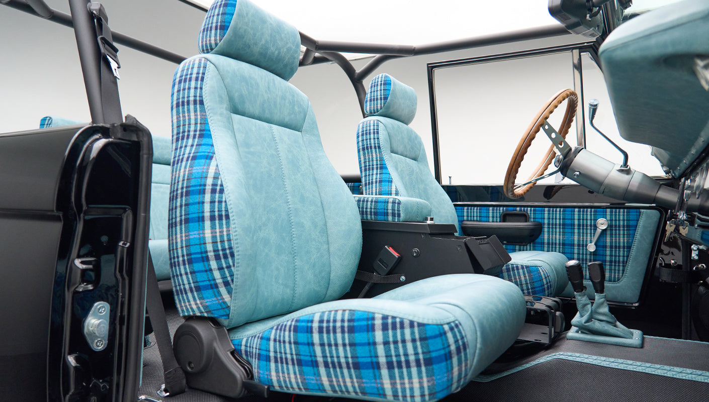 Front seats inside Classic Ford Bronco with blue plaid upholstery and roll cage