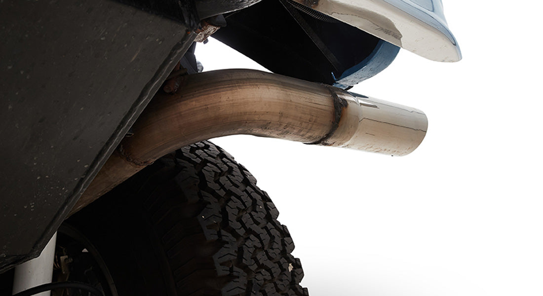 Exhaust pipe extending past rear tire of Classic Ford Bronco, showing part of blue body and white bumper.