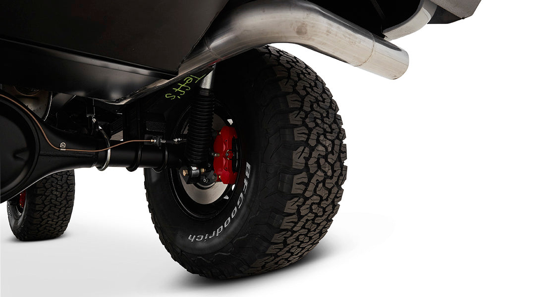 Underside view showing exhaust pipe, rear axle, red brake caliper, and off-road tire