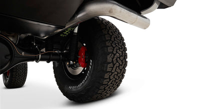 Underside view showing exhaust pipe, rear axle, red brake caliper, and off-road tire