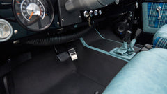 Floor area with pedals, controls, and blue plaid seats inside Classic Ford Bronco