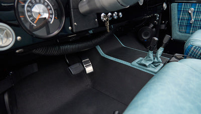 Floor area with pedals, controls, and blue plaid seats inside Classic Ford Bronco