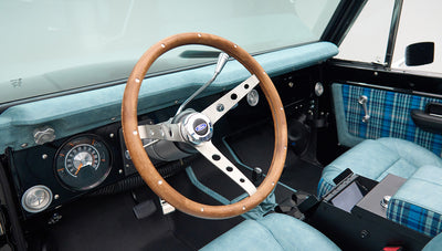 Classic Ford Bronco interior featuring wood steering wheel and blue upholstery with plaid inserts