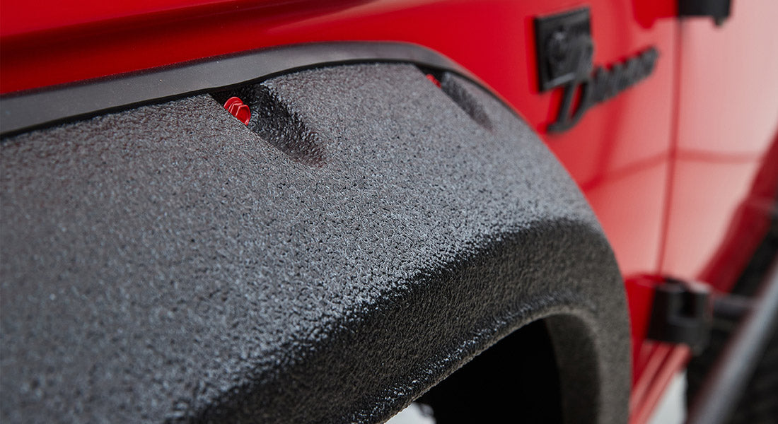 Textured black fender flare on red Classic Ford Bronco body near the wheel well edge