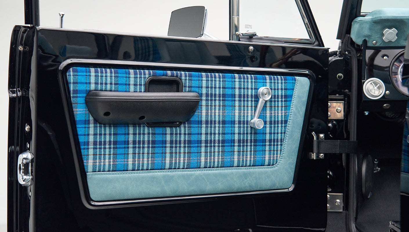 Close-up of Classic Ford Bronco door panel with blue plaid fabric and manual window crank