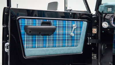 Close-up of Classic Ford Bronco door panel with blue plaid fabric and manual window crank