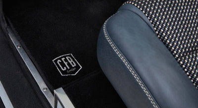 Black carpet floor mat with stitched CFB Series logo next to gray and black patterned car seat