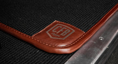 Close-up of black carpet floor mat with brown leather trim branded CFB Series