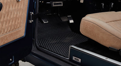 Interior floor mat and tan seat cushion with part of pedal cluster in a Classic Ford Bronco