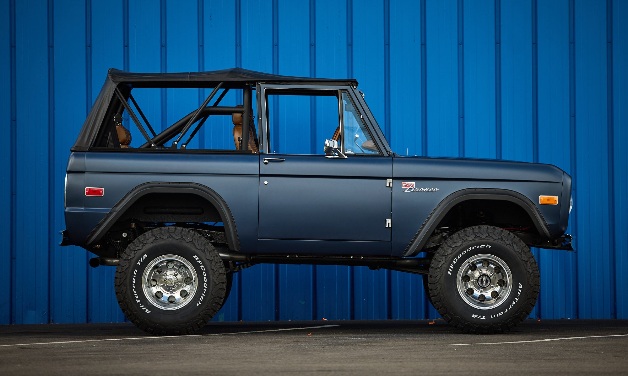 Classic Ford Bronco in matte navy blue with black soft top seen from passenger side