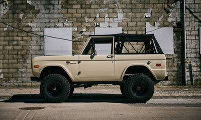 Side view of Classic Ford Bronco 1971 Quicksand color with black soft top and large tires