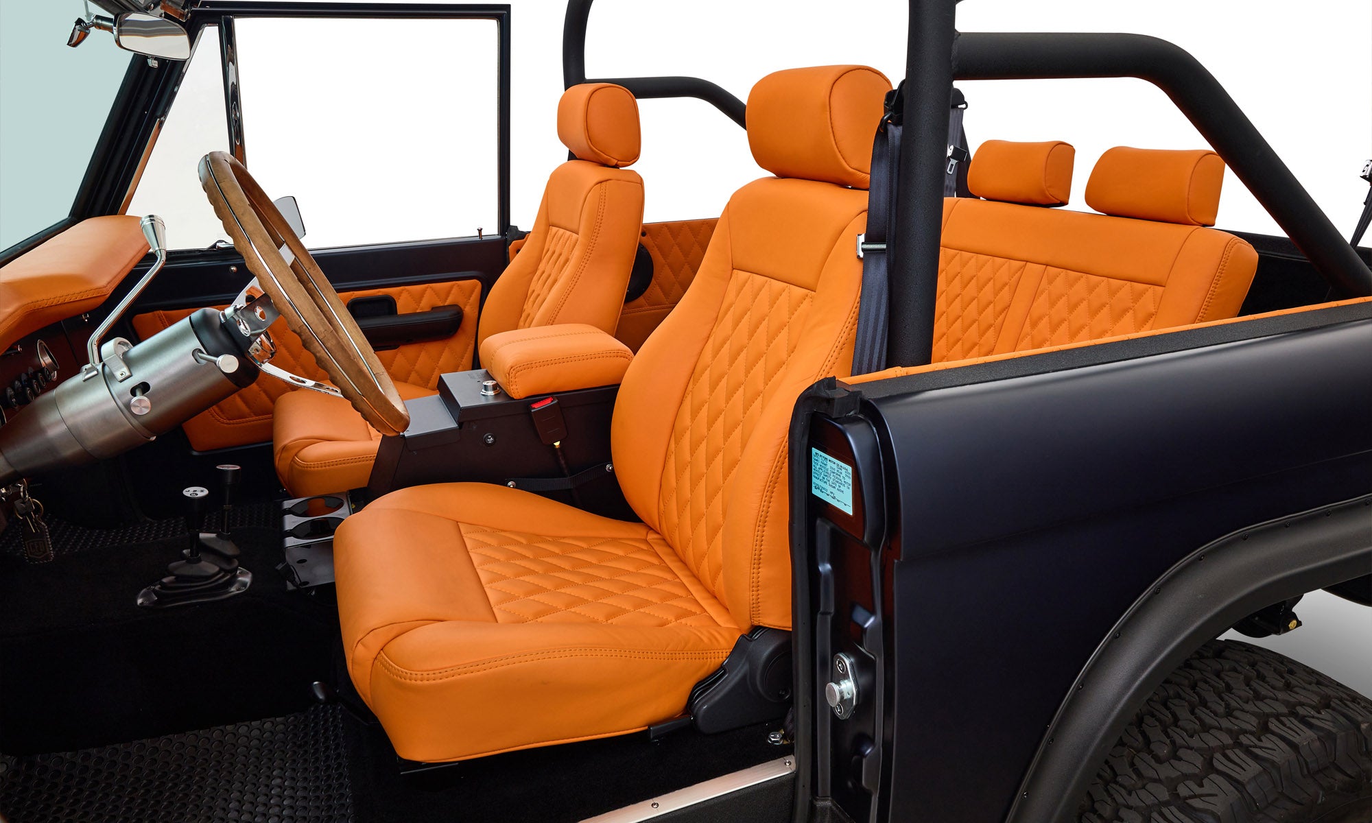 Interior of Classic Ford Bronco with matte navy exterior, featuring orange quilted seats and steering wheel