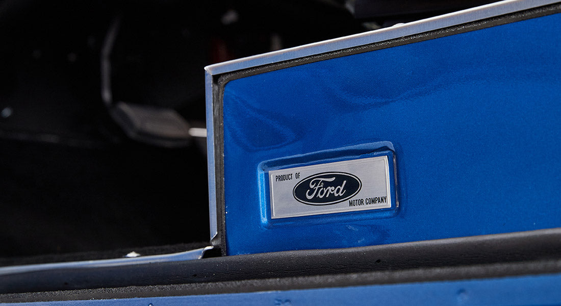 Silver badge reading 'Product of Ford Motor Company' on blue vehicle interior edge
